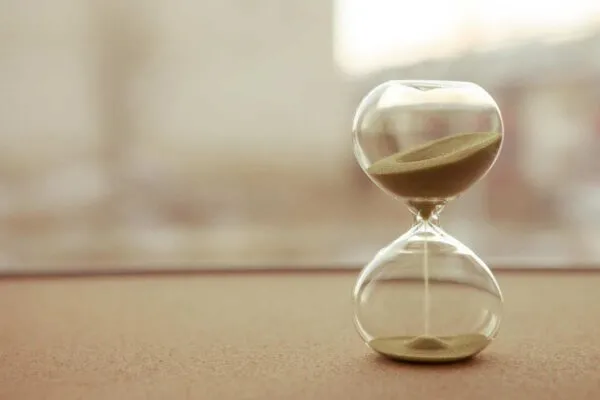 Sand running through the bulbs of an hourglass measuring the passing time in a countdown to a deadline, on a blur background | Dealing with “Time is of the Essence”